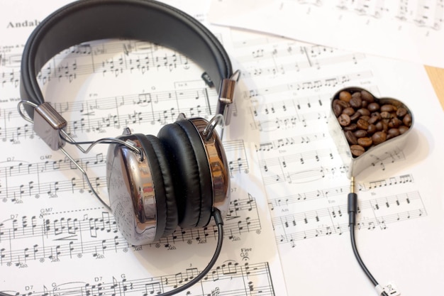 Vista de ángulo alto de auriculares con granos de café y partituras de música en la mesa