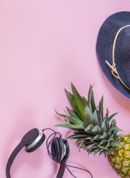 Foto vista de ángulo alto de auriculares por piña y sombrero en fondo rosa