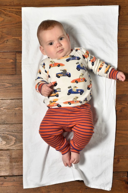 Vista de ángulo alto de un bebé en el piso de parquet vestido, serio y mirando al frente