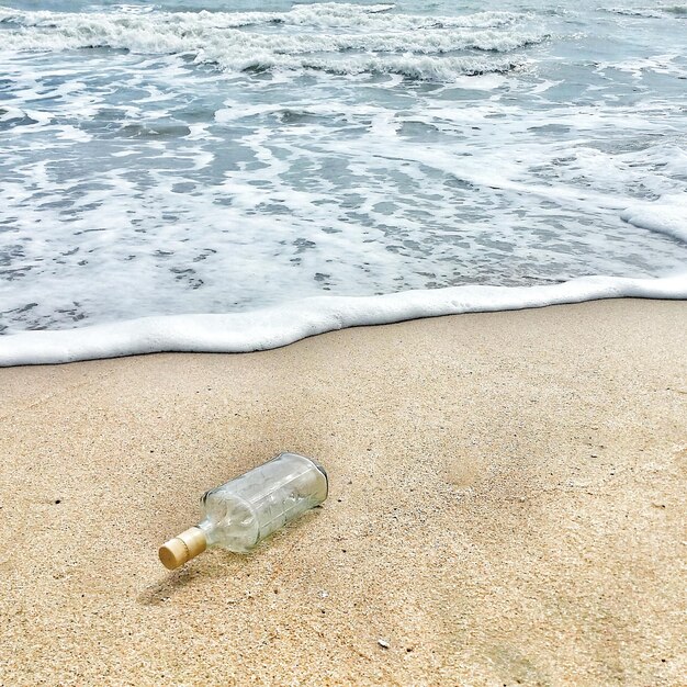 Foto vista de ángulo alto de una botella de cerveza vacía en la playa