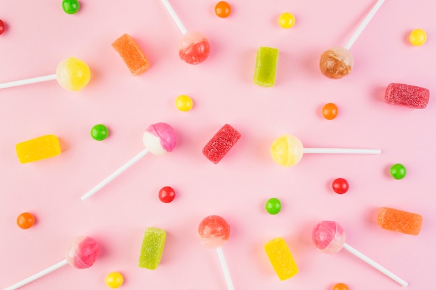 Foto vista de ángulo alto de caramelos de colores y piruletas en superficie rosa