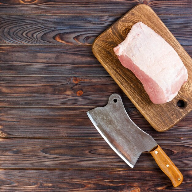 Foto vista de ángulo alto de carne cruda con tabla de cortar y cuchillo en la mesa