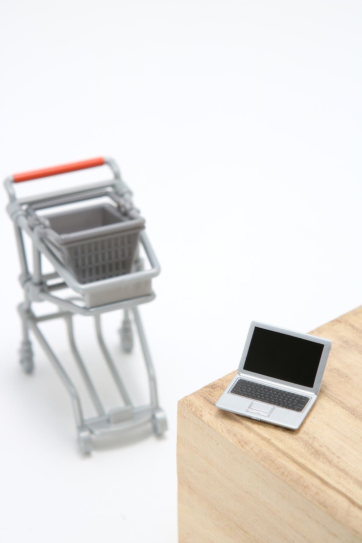 Foto vista de ángulo alto de una computadora portátil de juguete en la mesa por el carrito de compras contra un fondo blanco