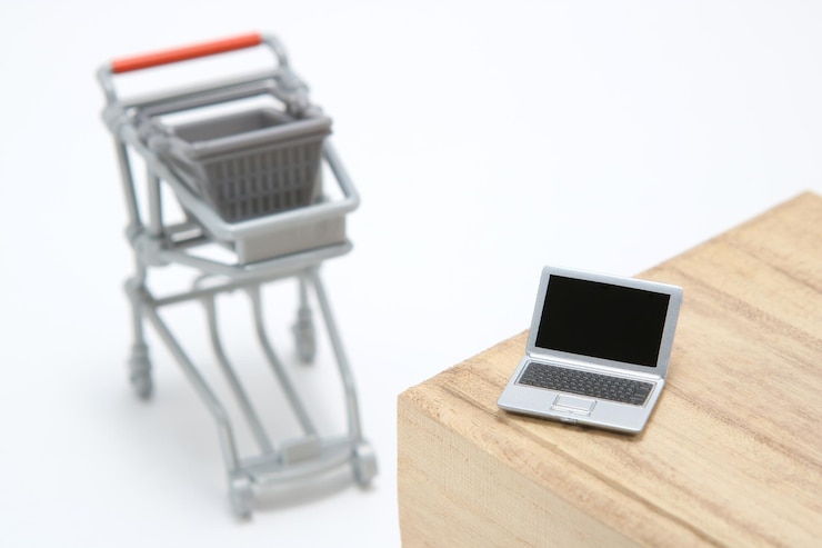 Foto vista de ángulo alto de una computadora portátil de juguete en la mesa por el carrito de compras contra un fondo blanco