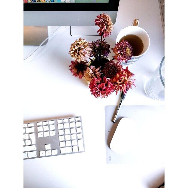 Foto vista de ángulo alto de las flores y la computadora en la mesa.