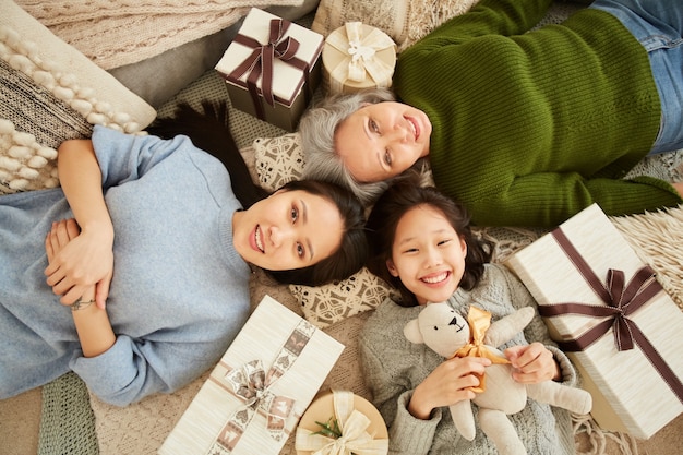 Vista de ángulo alto de la generación de la familia asiática tirada en el suelo entre regalos y juguetes y sonriendo