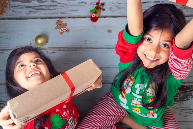 Vista de ángulo alto de hermanas sonrientes sosteniendo regalos mientras están sentadas en el piso de madera dura