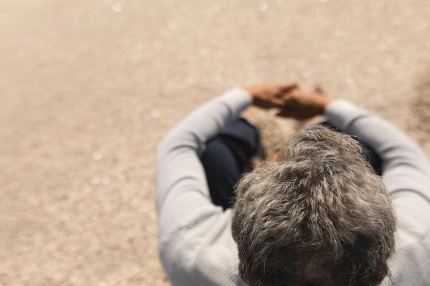 Vista de ángulo alto de un hombre mayor birracial con cabello gris sentado en la playa en un día soleado