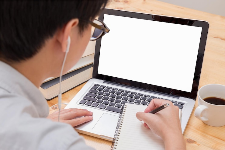 Foto vista de ángulo alto de un hombre de negocios escribiendo una nota mientras usa una computadora portátil en el escritorio