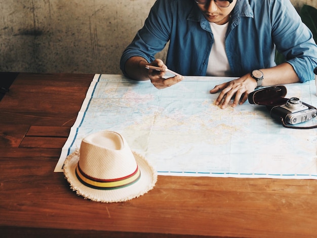 Foto vista de ángulo alto de un hombre con teléfono inteligente mirando el mapa del mundo en la mesa