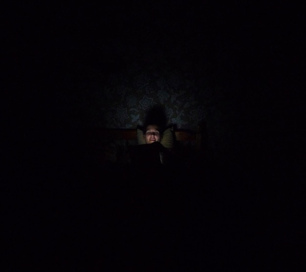 Foto vista de ángulo alto de un hombre usando el teléfono móvil en la cama en el cuarto oscuro