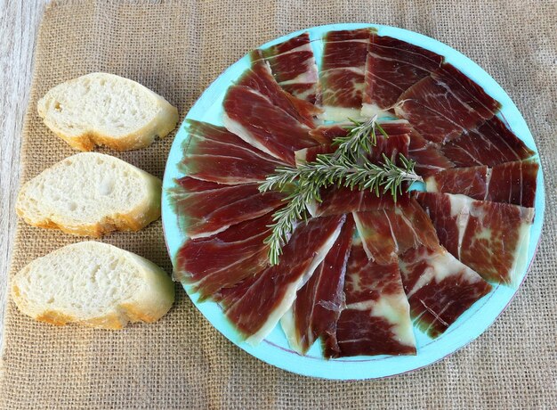 Foto vista de ángulo alto del jamón en un plato azul y algunos pedazos de pan