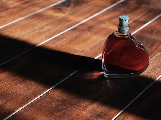 Vista de ángulo alto de líquido rojo en forma de corazón botella en el suelo de madera dura