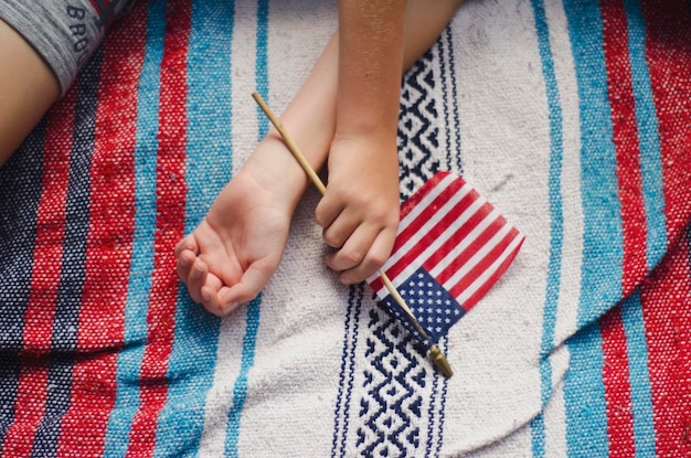 Foto vista de ángulo alto de la mano sosteniendo la bandera estadounidense mientras está acostada en la cama