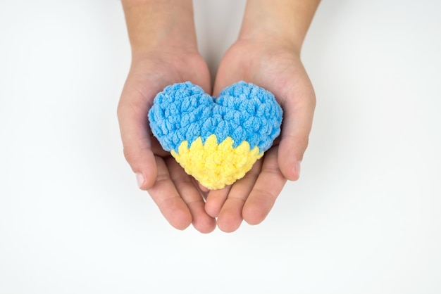 Vista de ángulo alto de las manos de los niños sosteniendo un corazón pintado en los corazones de la bandera ucraniana en las manos sobre un fondo blanco Concepto patriótico Me encanta Ucrania