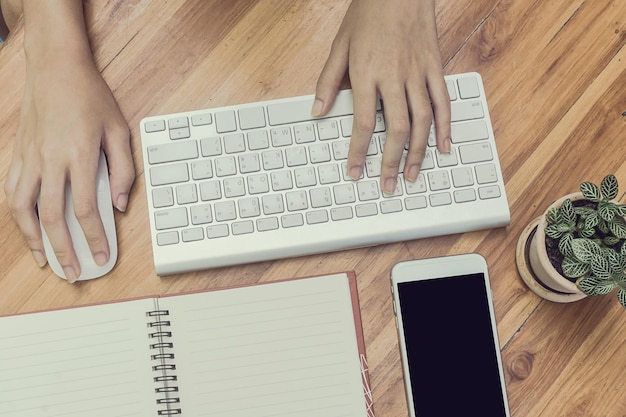 Vista de ángulo alto de las manos de la persona usando el ratón y el teclado de la computadora en la mesa