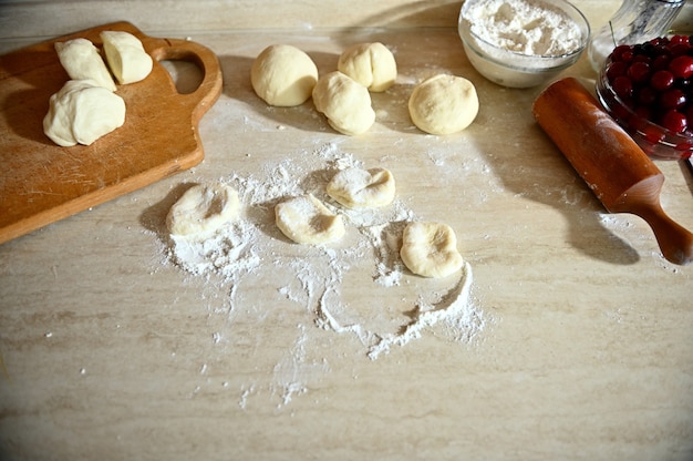 Vista de ángulo alto de masa sobre encimera de cocina y tablero de madera con rodillo acostado sobre la encimera de la cocina con harina esparcida. Proceso de cocción de albóndigas paso a paso.