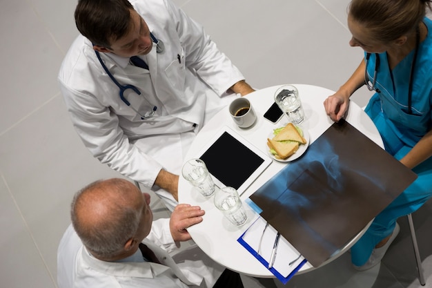 Vista de ángulo alto de médicos y cirujanos examinando rayos X mientras desayuna