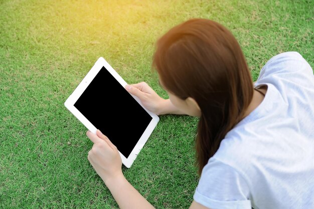 Vista de ángulo alto de una mujer adulta usando una tableta digital mientras yace en un campo de hierba en el parque