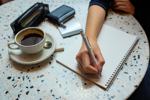 Vista de ángulo alto de una mujer escribiendo en el bloc de notas por la taza de café en la mesa