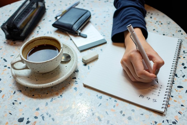 Vista de ángulo alto de una mujer escribiendo en el bloc de notas por la taza de café en la mesa