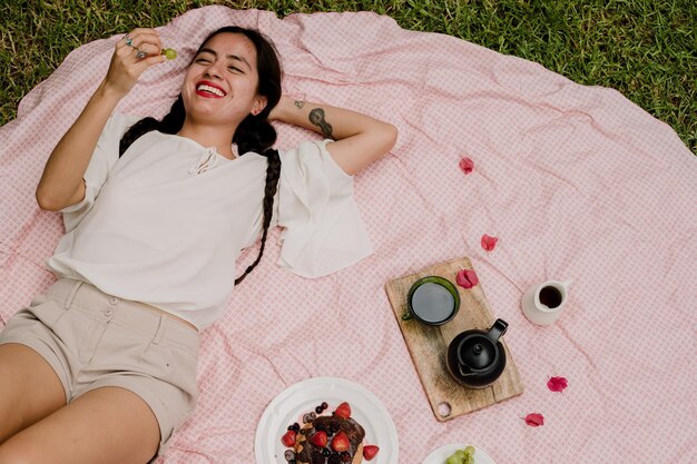 Vista de ángulo alto de una mujer con frutas mientras yace en una manta de picnic en el patio