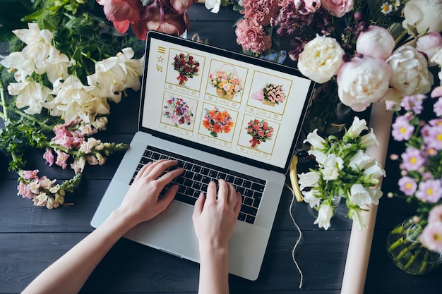 Vista de ángulo alto de una mujer irreconocible usando una computadora portátil mientras agrega flores al carrito en la tienda mayorista web, concepto de tienda de flores