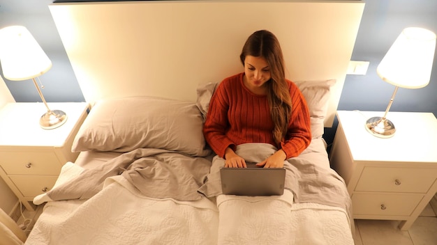 Vista de ángulo alto de una mujer joven usando una computadora portátil en la cama