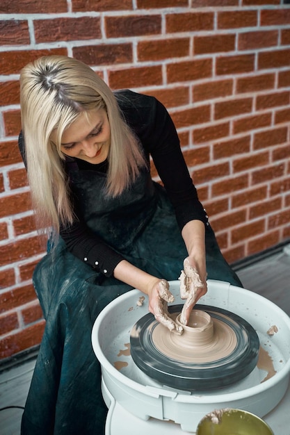 Foto vista en ángulo alto de una mujer moldeando arcilla en una rueda de cerámica