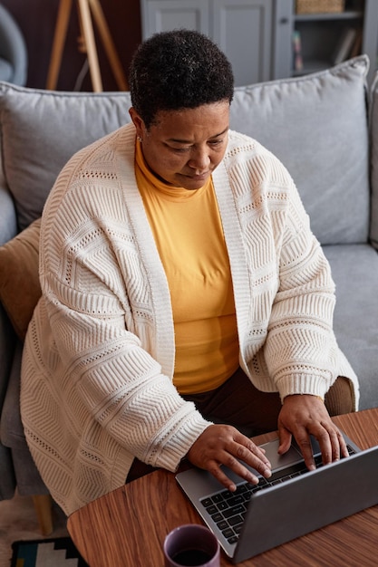 Vista de ángulo alto en la mujer negra mayor que usa una computadora portátil mientras trabaja desde casa en línea