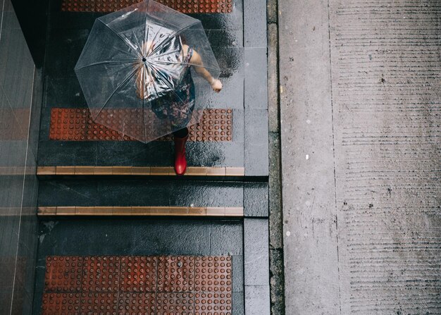 Foto vista de ángulo alto de una mujer con un paraguas transparente caminando por la acera durante la temporada de lluvias