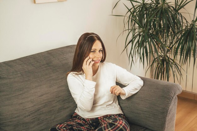 Vista de ángulo alto de una mujer sonriente hablando en un teléfono inteligente mientras está sentada en el sofá en casa