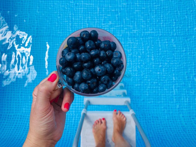 Foto vista de ángulo alto de una mujer sosteniendo arándanos sobre la piscina