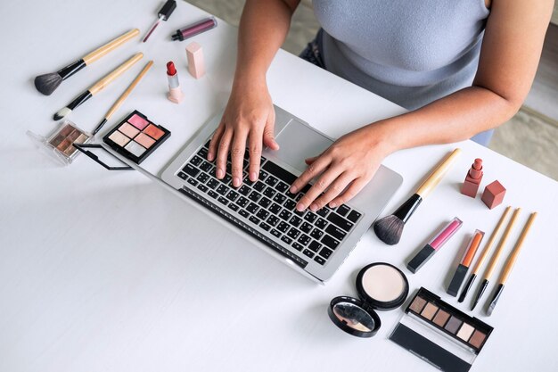 Vista de ángulo alto de una mujer usando una computadora portátil por productos de belleza en la mesa