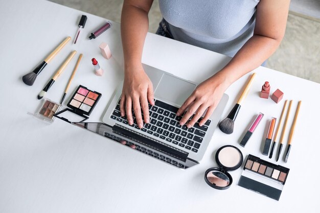Vista de ángulo alto de una mujer usando una computadora portátil por productos de belleza en la mesa