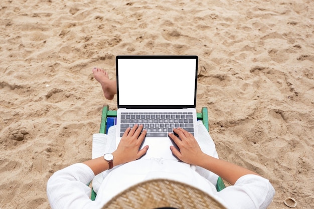 Foto vista de ángulo alto de una mujer usando una computadora portátil en una silla en la playa