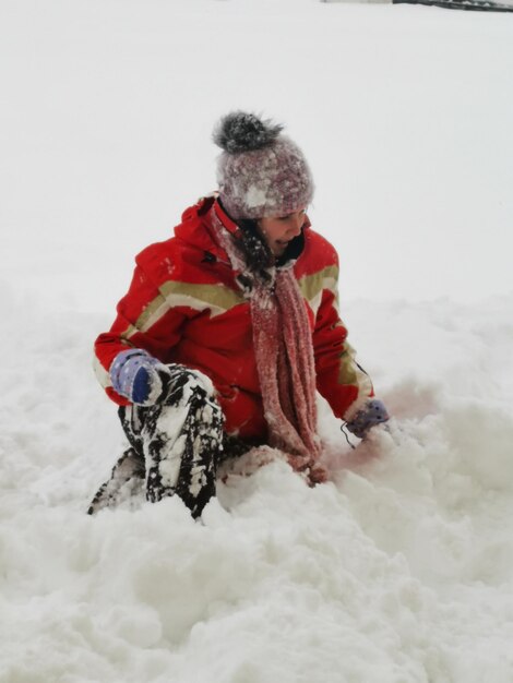 Vista de ángulo alto de una niña sentada en un campo cubierto de nieve