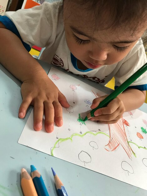 Vista de ángulo alto de un niño dibujando en papel en la mesa