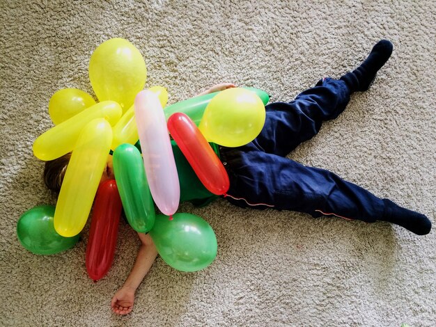 Foto vista de ángulo alto de un niño con globos coloridos mientras está acostado en la alfombra en casa