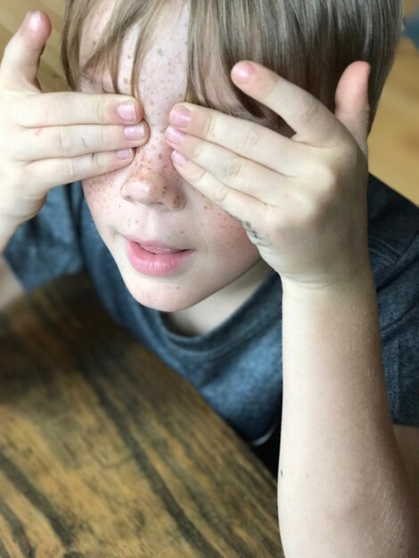 Foto vista de ángulo alto de un niño juguetón cubriendo sus ojos en casa