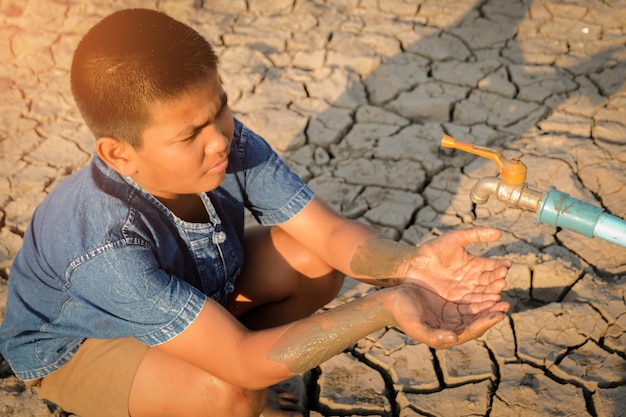 Foto vista de ángulo alto de un niño sentado bajo un grifo en una tierra seca