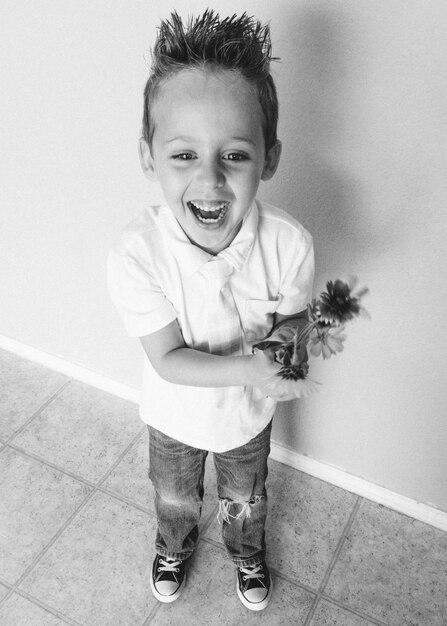 Foto vista de ángulo alto de un niño sonriente de pie con flores en casa