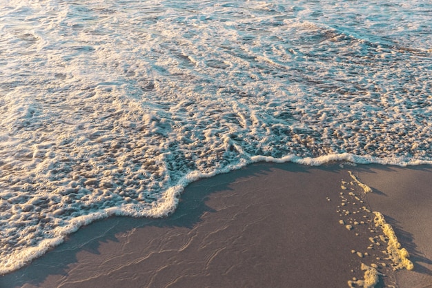 Vista de ángulo alto de las olas del mar salpicando en la playa durante la puesta del sol. Copiar el espacio, la costa, el surf, la naturaleza y el concepto de movimiento.