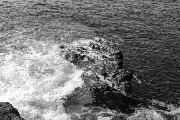 Foto vista de ángulo alto de las olas salpicando y chocando contra y sobre las rocas surf de agua blanca