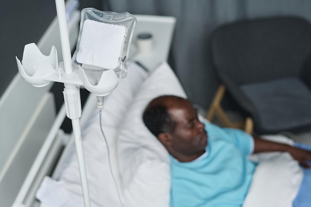 Vista de ángulo alto del paciente afroamericano con cuentagotas acostado en la cama en la sala del hospital