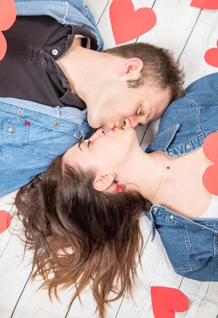 Foto vista de ángulo alto de una pareja con corazones de papel besándose mientras yacen en el suelo de madera