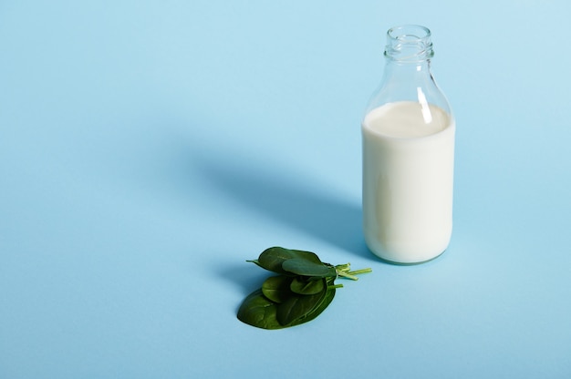 Vista de ángulo alto de una pequeña botella de vidrio con leche orgánica y hojas de espinaca