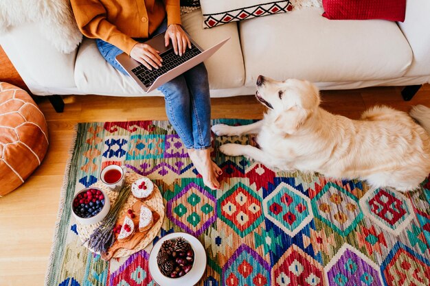 Foto vista de ángulo alto de un perro mirando a una mujer usando una computadora portátil mientras está sentada en el sofá en casa