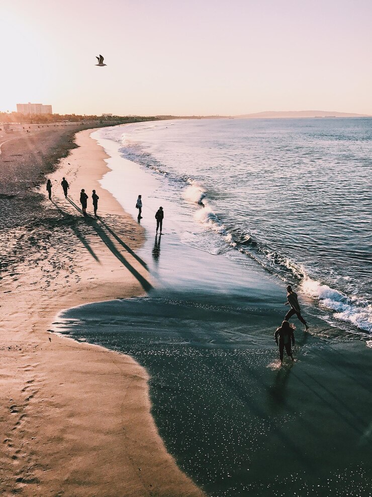 Vista de ángulo alto de personas disfrutando en la playa contra el cielo durante la puesta de sol