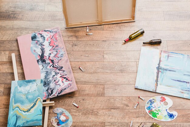 Vista de ángulo alto de pinturas dibujar utensilios y botellas vacías en el piso de madera en el estudio de pintura